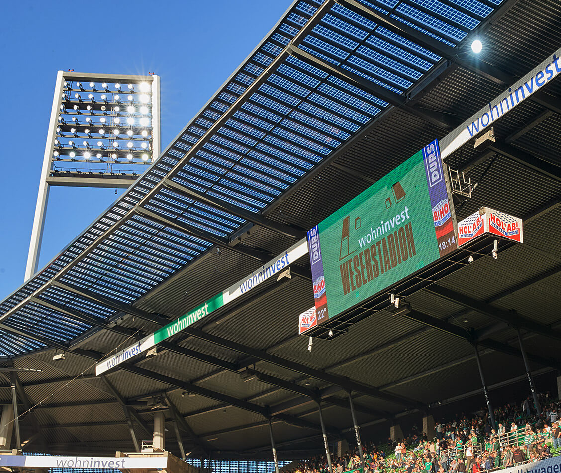 This picture shows the LED wall with the wohninvest WESERSTADION logo and the roof wreath with the Wohninvest logo.